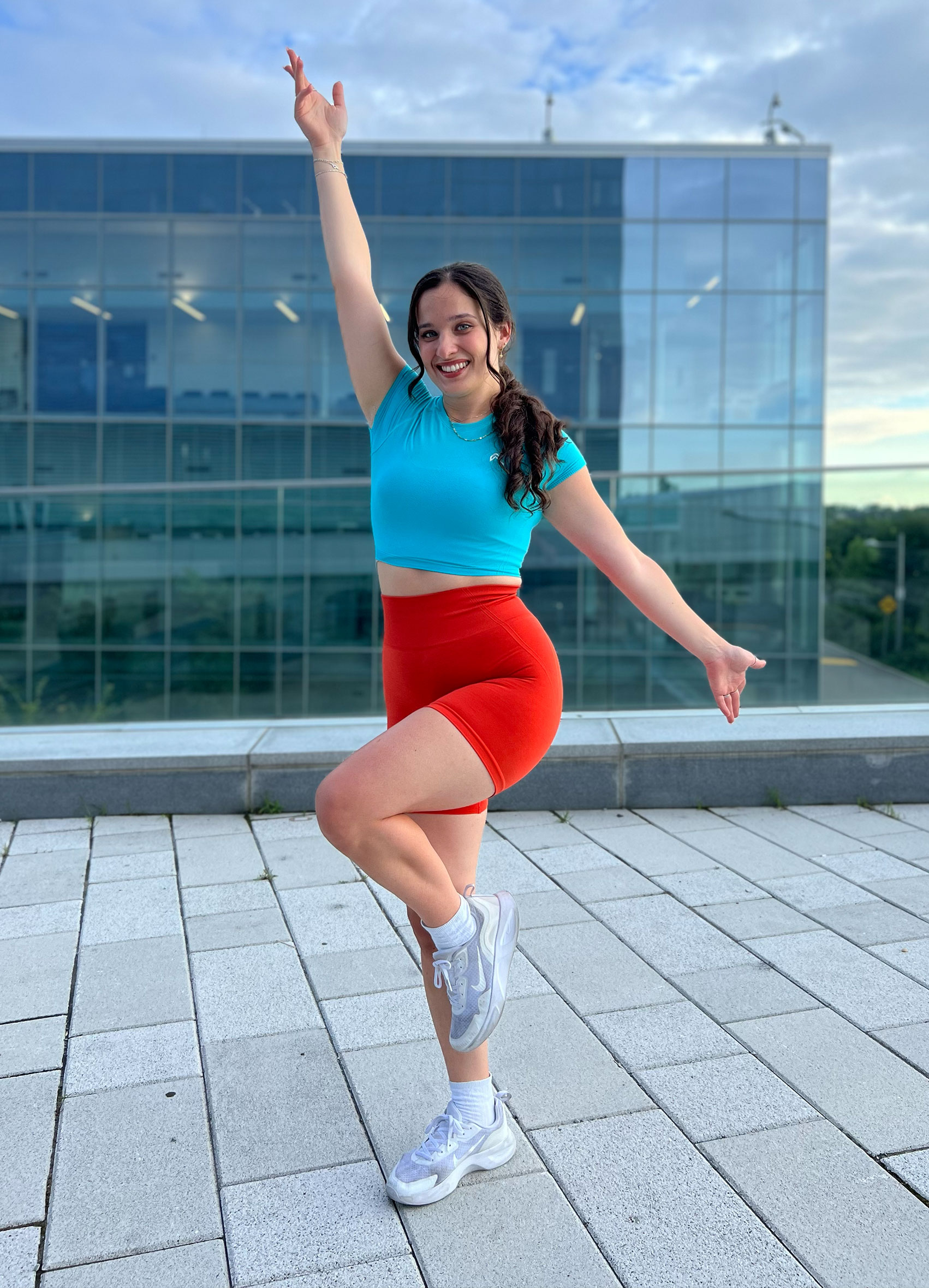 Coach posing outside while smiling, wearing fitness clothes